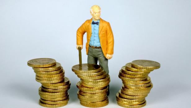 Eine Spielfigur eines älteren Mannes steht hinter drei Stapeln von Goldmünzen.