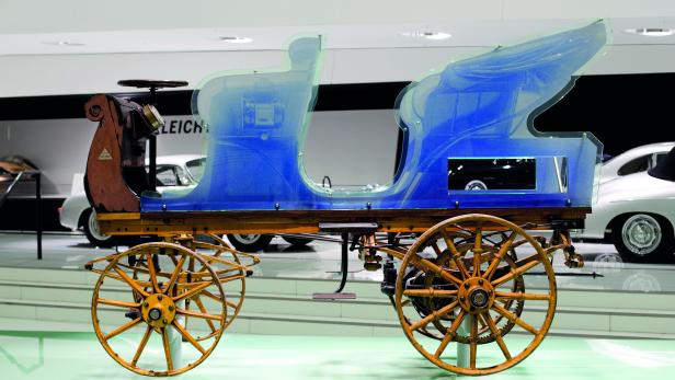 Ein historischer Wagen mit Holzrädern und einer transparenten blauen Karosserie steht in einem Museum.