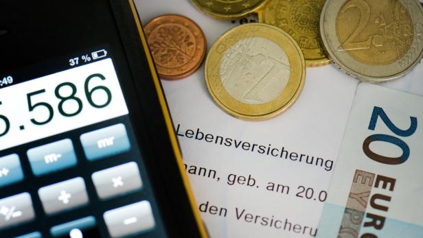 Ein Taschenrechner, Euro-Münzen und ein 20-Euro-Schein liegen auf einem Dokument zur Lebensversicherung.