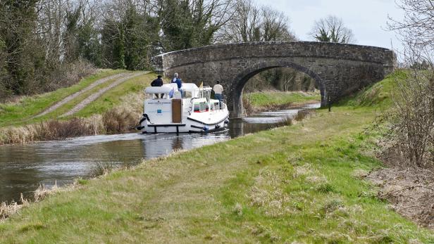 Ein kleines Boot fährt unter einer Steinbrücke auf einem Kanal hindurch.
