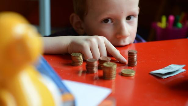 Ein kleiner Junge zählt sein Geld auf einem roten Tisch.