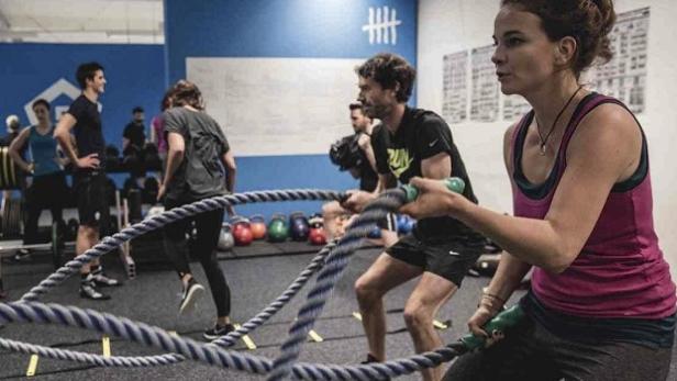 Eine Frau trainiert mit einem Battle Rope in einem Fitnessstudio, während andere trainieren.
