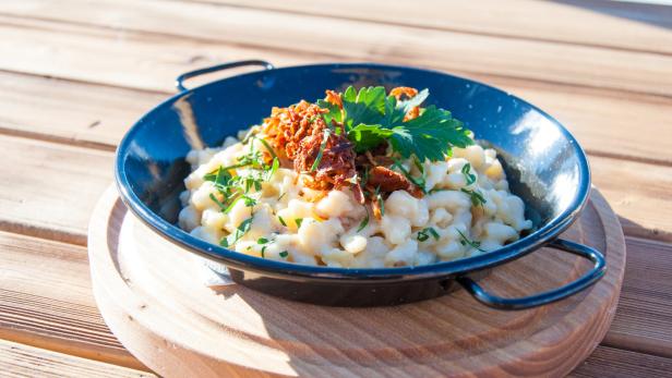 Eine Portion Käsespätzle mit Röstzwiebeln und Petersilie in einer schwarzen Pfanne.