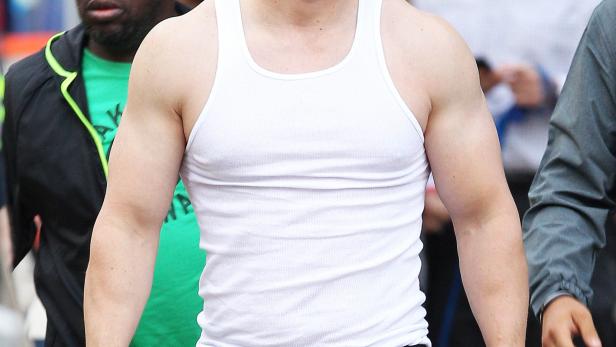 Mark Wahlberg in einem weißen Tanktop und schwarzen Hosen hält eine Wasserflasche.