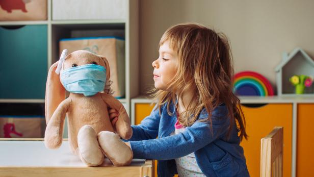 Little girl playing with rabbit soft toy in the medicine mask