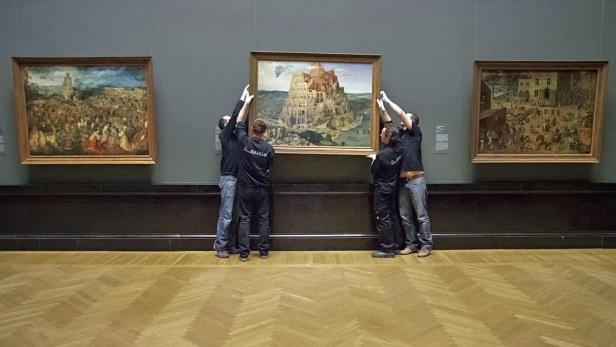 Vier Personen hängen ein Gemälde des Turms zu Babel in einem Museum auf.