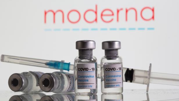 Vials labelled "COVID-19 Coronavirus Vaccine" and sryinge are seen in front of displayed Moderna logo in this illustration