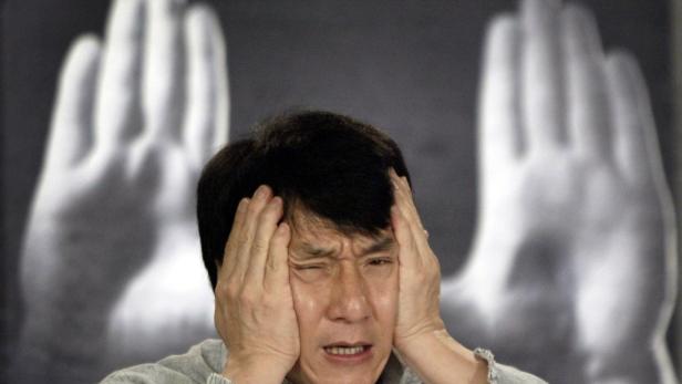 Jackie Chan hält sich mit schmerzverzerrtem Gesicht die Hände an den Kopf.
