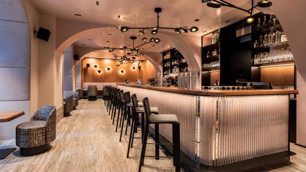 Eine Bar mit Hockern und einer beleuchteten Theke in einem eleganten Interieur.