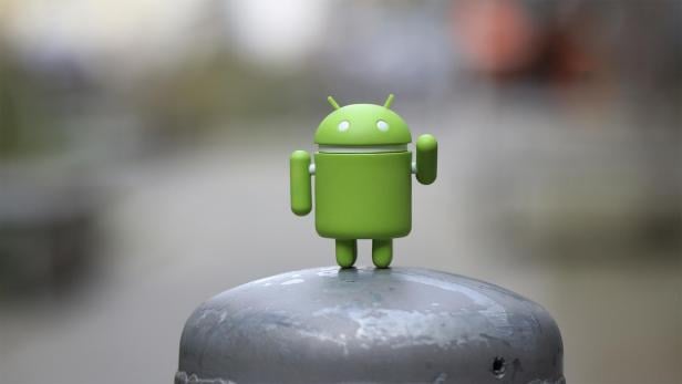 Eine grüne Android-Figur steht auf einem grauen, metallischen Untergrund.