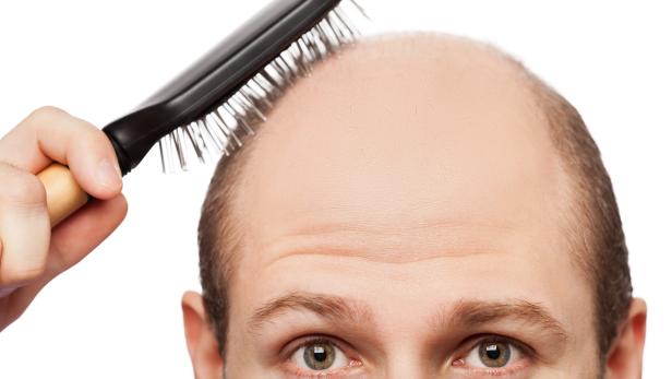 Bald man attempting to use hairbrush