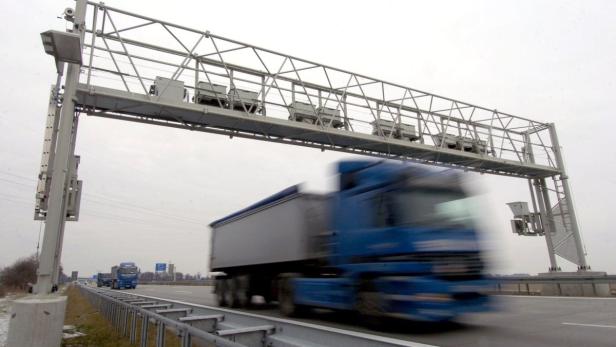 Ein blauer LKW fährt unter einer Mautbrücke auf einer Autobahn hindurch.