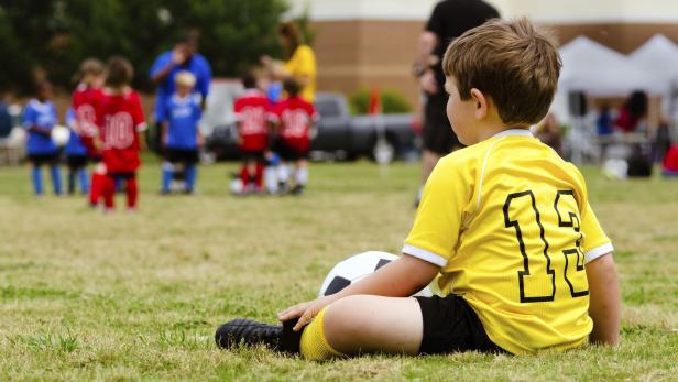 Young boy child in uniform watching organized youth soccer or football game from sidelines