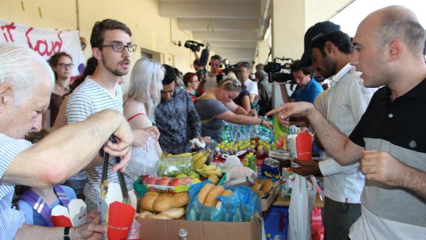 Menschen stehen an einem Tisch mit Lebensmitteln und Getränken, während Kameras sie filmen.