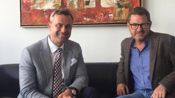 Zwei Männer sitzen auf einer Couch vor einem abstrakten Gemälde.