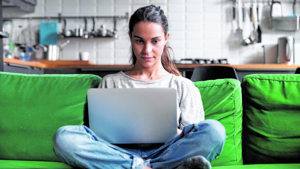 Eine Frau sitzt mit einem Laptop auf einem grünen Sofa.