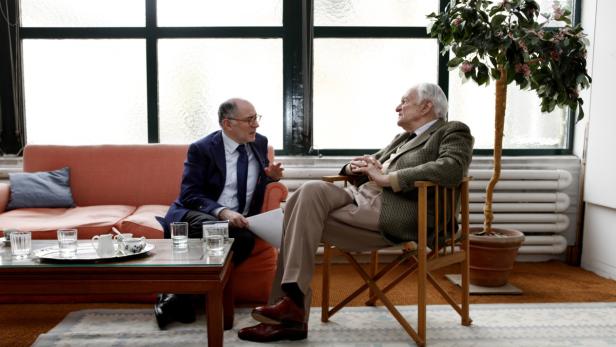 Zwei Männer sitzen in einem Wohnzimmer und unterhalten sich.