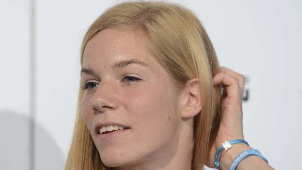 Eine blonde Frau mit blauem Armband berührt ihr Haar.