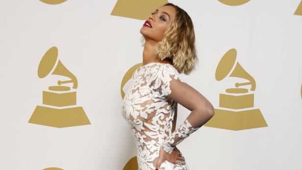 Beyoncé posiert auf dem roten Teppich vor einer Wand mit goldenen Grammy-Logos.