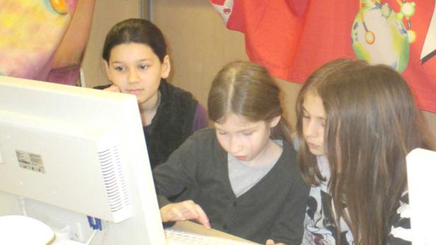Drei Mädchen sitzen vor einem Computer und schauen auf den Bildschirm.