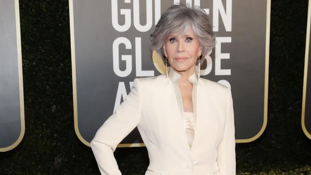 Jane Fonda in einem weißen Hosenanzug auf dem roten Teppich.