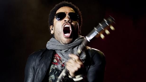 Lenny Kravitz tritt mit Sonnenbrille und Gitarre auf einer Bühne auf.