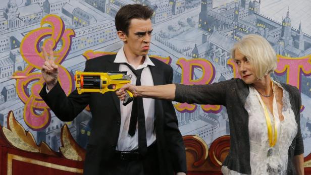 Helen Mirren zielt mit einer Spielzeugpistole auf einen Mann in einem Anzug.