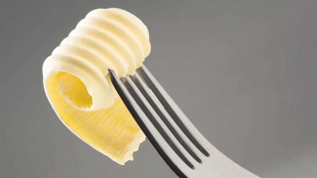 Eine Butterrolle auf einer Gabel vor grauem Hintergrund.
