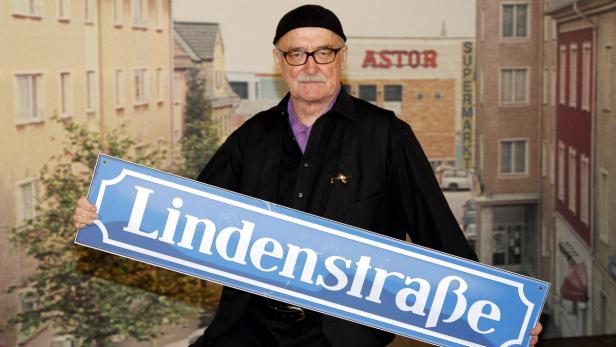 Ein Mann hält ein blaues Straßenschild mit der Aufschrift „Lindenstraße“.