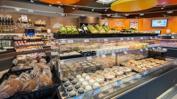In einem Supermarktregal werden Brot, Salate und Getränke angeboten.
