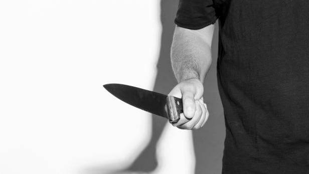 Man in black t-shirt, standing holding a knife.