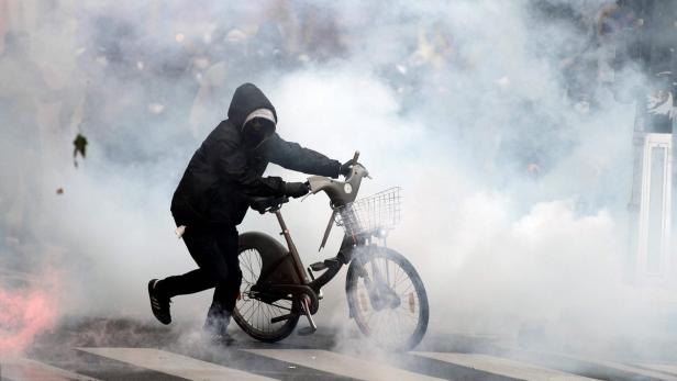 Eine Person mit Kapuze schiebt ein Fahrrad durch eine Rauchwolke.