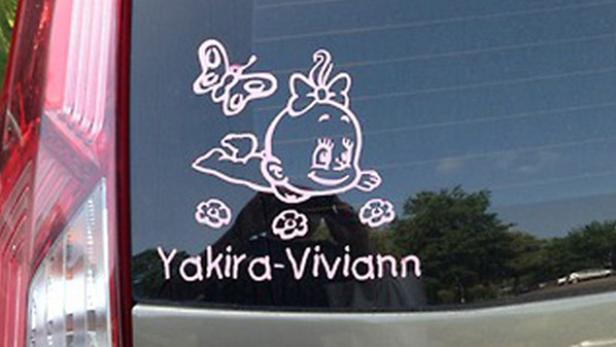 Ein Autoaufkleber zeigt ein Baby, einen Schmetterling, Blumen und den Namen Yakira-Viviann.
