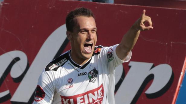 Ein jubelnder Fußballspieler in weißem Trikot zeigt mit dem Finger nach oben.