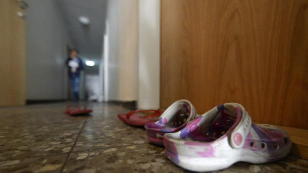 Ein Paar bunte Clogs und Sandalen stehen in einem Flur vor einer Holztür.