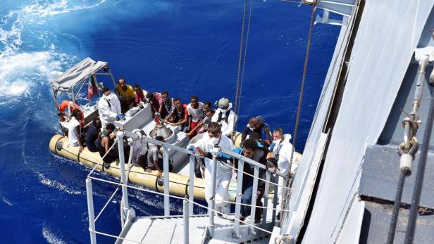 Ein Schlauchboot mit Menschen wird an Bord eines Schiffes gebracht.