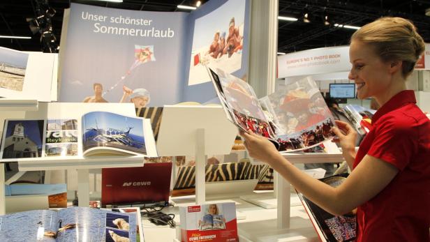 Eine Frau betrachtet ein Fotobuch auf einem Messestand von CEWE mit dem Slogan „Unser schönster Sommerurlaub“.