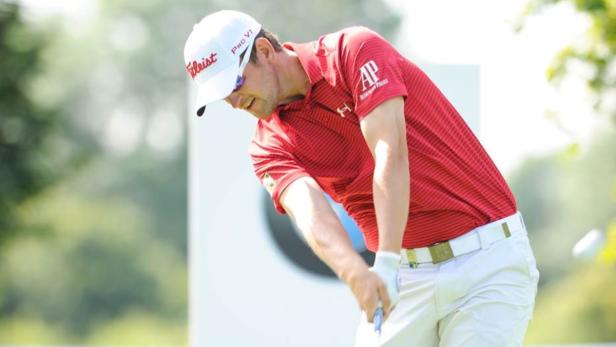 Ein Golfspieler in rotem Hemd und weißer Hose beim Abschlag.