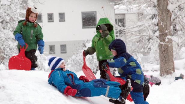 Eine Gruppe Kinder spielt mit Schlitten im Schnee.
