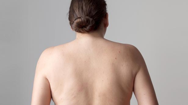 Die Rückansicht einer Frau mit hochgesteckten Haaren vor einem grauen Hintergrund.