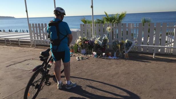 Ein Radfahrer steht vor einer Gedenkstätte mit Blumen und Kerzen am Strand.