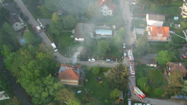 Rauch steigt aus einem Haus, während Feuerwehrwagen in einer Wohngegend eintreffen.
