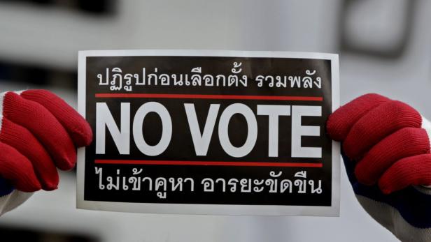 Zwei Hände mit roten Handschuhen halten ein Schild mit der Aufschrift „No Vote“.