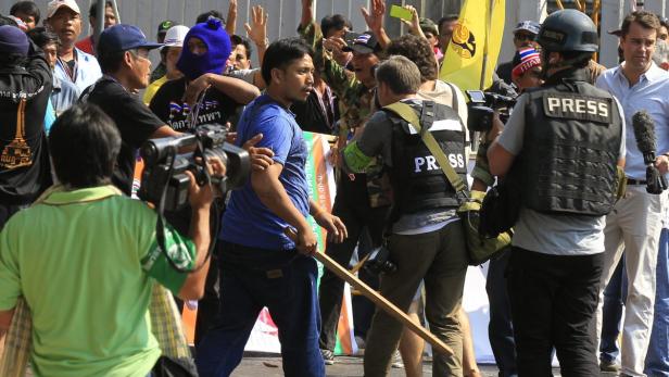 Eine Menschenmenge umringt Journalisten und einen Mann mit einem Stock in der Hand.