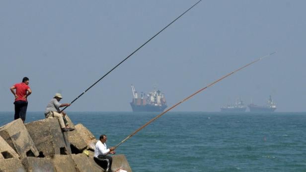 Men fish as Libyan-chartered ship Amalthea carrying aid for Palestinians in Gaza sails in El Arish port, 344 km (214 miles) northeast of Cairo, before unloading its cargo, July 15, 2010. The ship reached the Egyptian port on Wednesday after altering its course following a warning from Israel&#039;s navy not to head to the blockaded Gaza Strip. REUTERS/Mohamed Abd El-Ghany (EGYPT - Tags: CIVIL UNREST POLITICS)