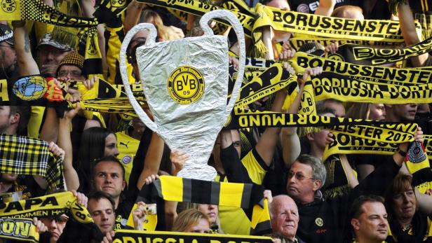 Fans von Borussia Dortmund feiern mit einem Pokalmodell und Schals.