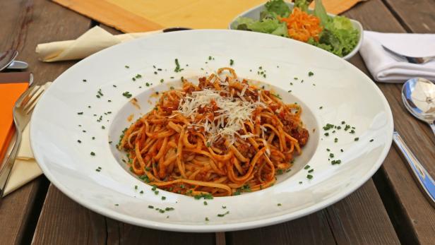Ein Teller Linguine Bolognese, garniert mit frischem Schnittlauch und geriebenem Käse, steht auf einem Holztisch.