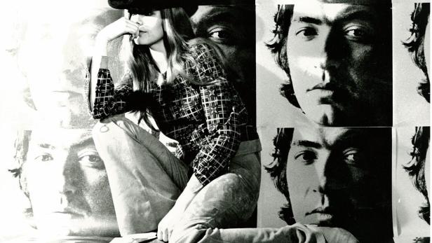 Eine Frau mit Hut posiert vor einem Hintergrund mit Porträts.