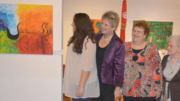 Vier Frauen betrachten ein farbenfrohes Gemälde mit arabischer Schrift in einer Kunstausstellung.