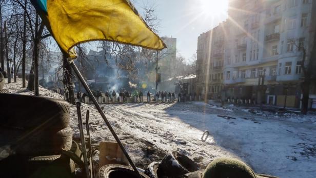 Eine ukrainische Flagge weht vor einer Barrikade auf einer verschneiten Straße.